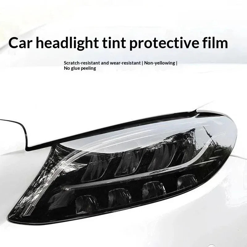 A close-up of a car headlight tinted with a protective film, showing a clear, dark lens on a white vehicle.