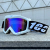 White windproof sports goggles with purple-blue mirrored lenses and a black strap resting on a gray stone surface.