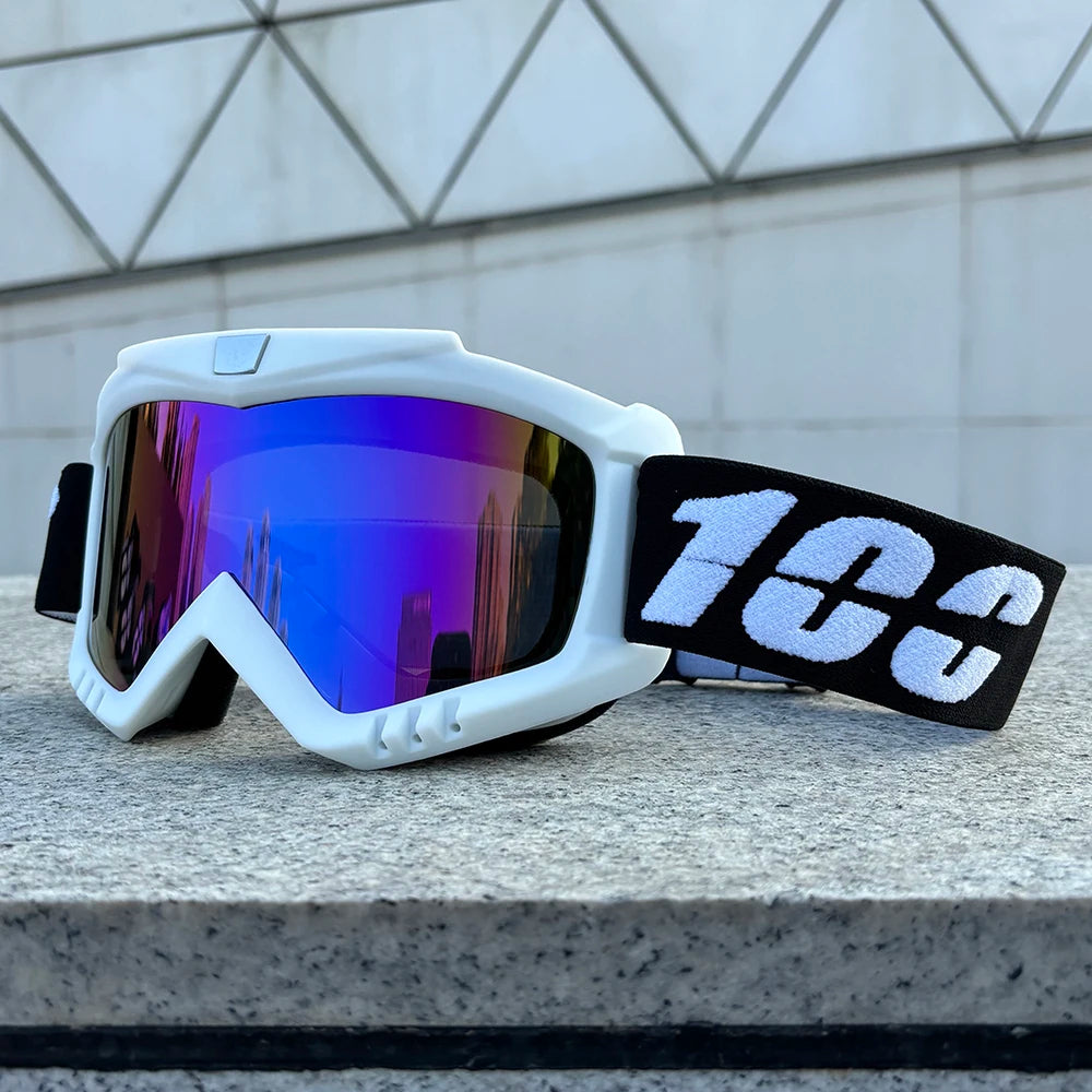 White windproof sports goggles with purple-blue mirrored lenses and a black strap resting on a gray stone surface.