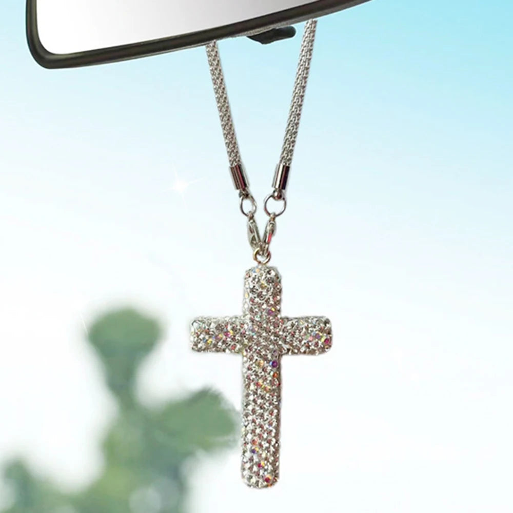 A sparkling stainless steel cross pendant hanging from a chain, displayed against a bright blue sky.