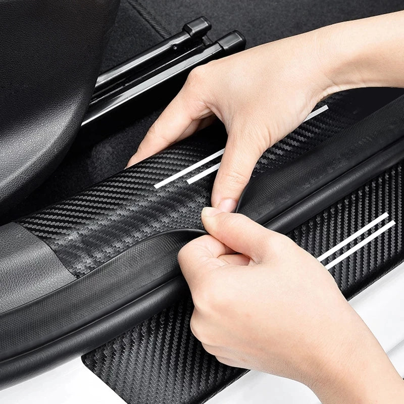 A hand is applying a carbon fiber protection decal to the surface of a car door or trunk.