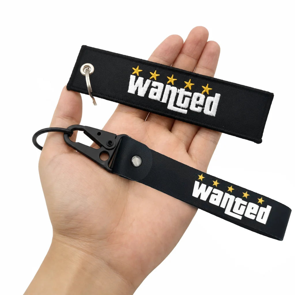 Porte-clés en nylon noir avec le mot 'wanted' brodé en étoiles blanches et jaunes