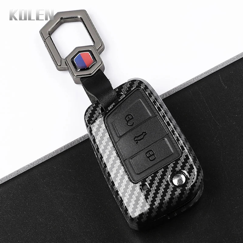 A black carbon fiber button cover for a car key, featuring a silver clasp and a red and blue accent.