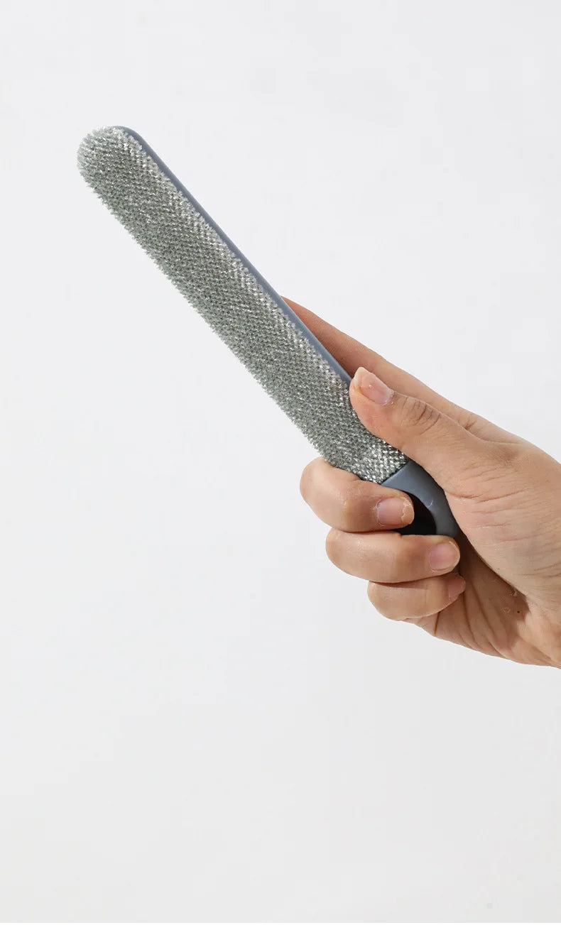 A hand holds a long-handled static pet hair remover brush with a gray bristled head.