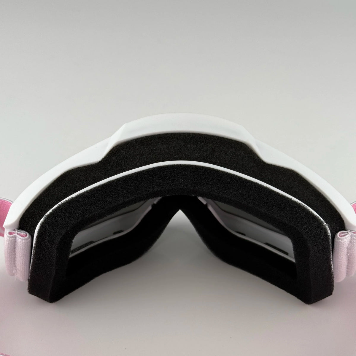A pair of black and white off-road motorcycle goggles with protective foam padding.