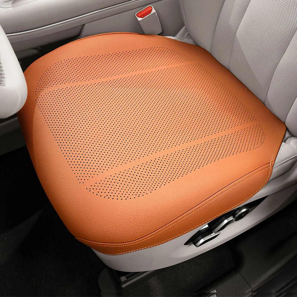 An orange breathable car seat cushion is shown placed in the interior of a vehicle.