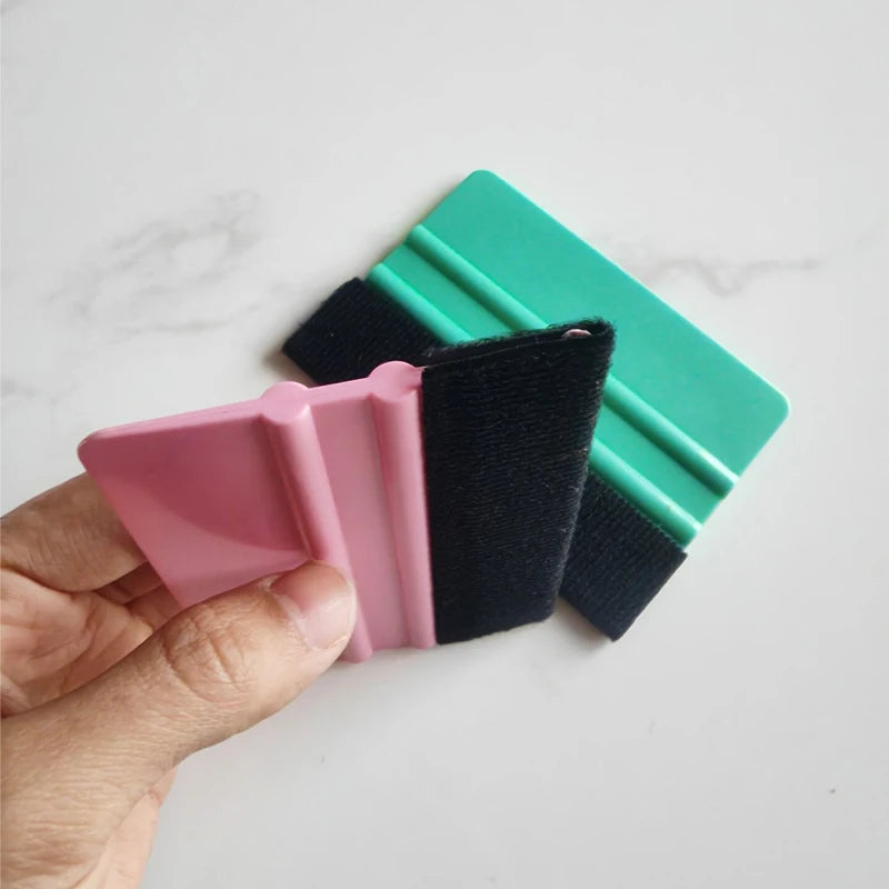 A hand holds a pink felt squeegee tool with a black strap and a green plastic handle.