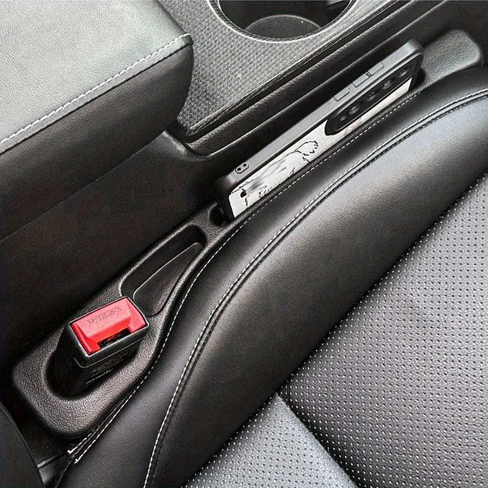 A close-up view of a car seat gap filler organizer with a red switch and a silver electronic component in a black car interio
