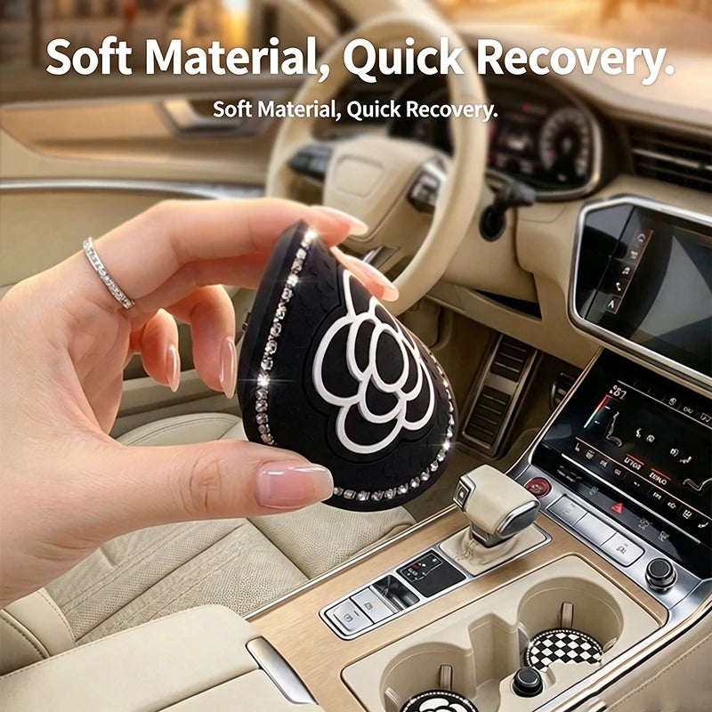 A hand holds a black silicone coaster with white floral designs in the interior of a car dashboard.