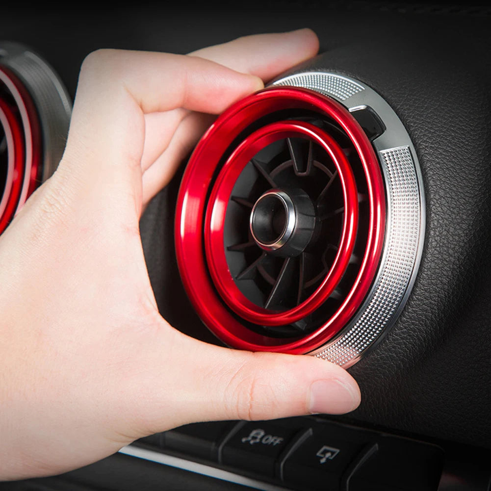 A hand is removing a red interior air vent trim cover from a car dashboard.