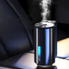 A black portable car air freshener device emitting white steam, resting on a surface.