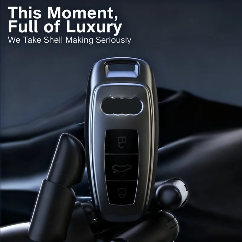 A close-up of a sleek, metallic car key case cover being held by a hand against a dark background.