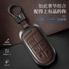 A dark brown genuine leather car key fob cover with a silver metal clasp and embossed panic buttons resting on a dark surface
