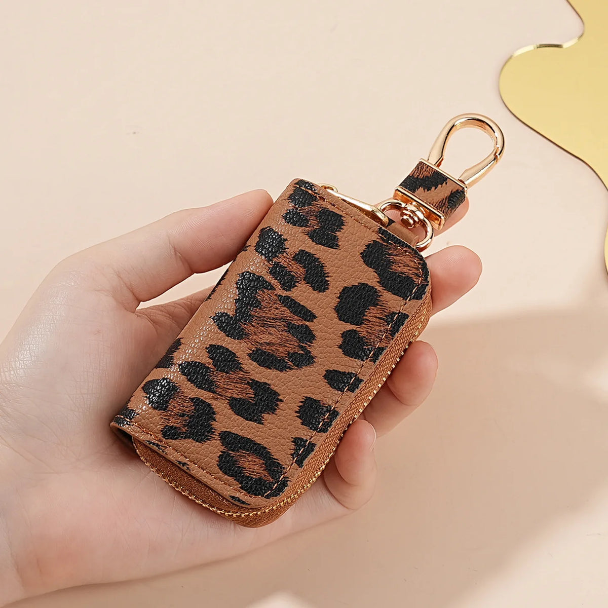 A hand holds a brown leopard print car key holder with a gold clasp against a light background.