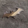Silberfarbiger 3D-Metall-Bat-Aufkleber-Abzeichen auf einer dunkelgrauen, strukturierten Oberfläche.
