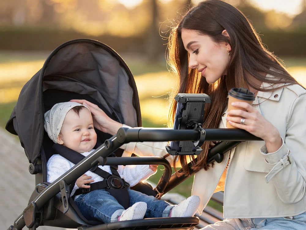 A woman is holding a baby in a bike phone holder with a hidden tracker for motorcycle safety during sunset.