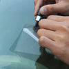 A hand is using a tool to repair a crack on a car window with a glass repair kit.