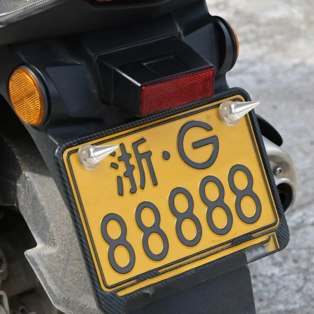 A close-up of a yellow license plate with black characters and silver screws mounted on a dark vehicle body.