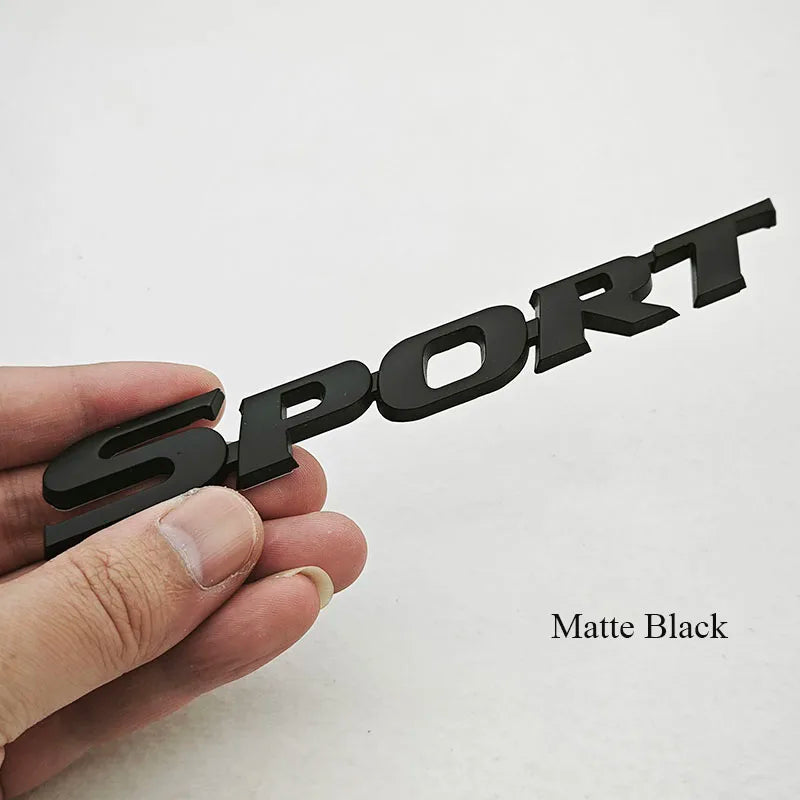 A hand holds a black 3D chrome car logo emblem for the rear trunk.