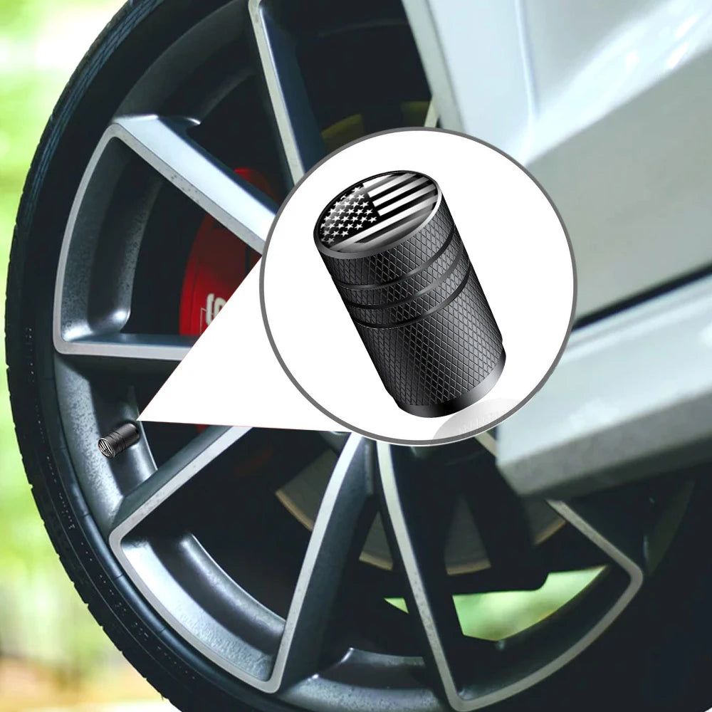 Close-up view of an American flag aluminum tire valve cap with a textured finish mounted on a wheel rim.