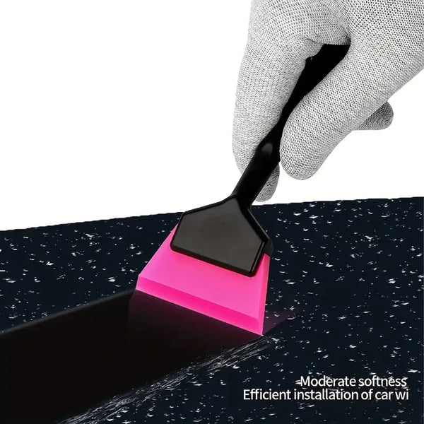 A hand is using a black installation tool with a pink rubber blade to apply film onto a dark surface.