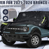 Schwarze wasserdichte Autoabdeckung schützt einen türkisen Ford Bronco mit vier Türen in einer verschneiten Außenumgebung.