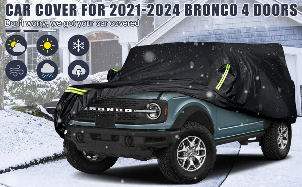 Schwarze wasserdichte Autoabdeckung schützt einen türkisen Ford Bronco mit vier Türen in einer verschneiten Außenumgebung.