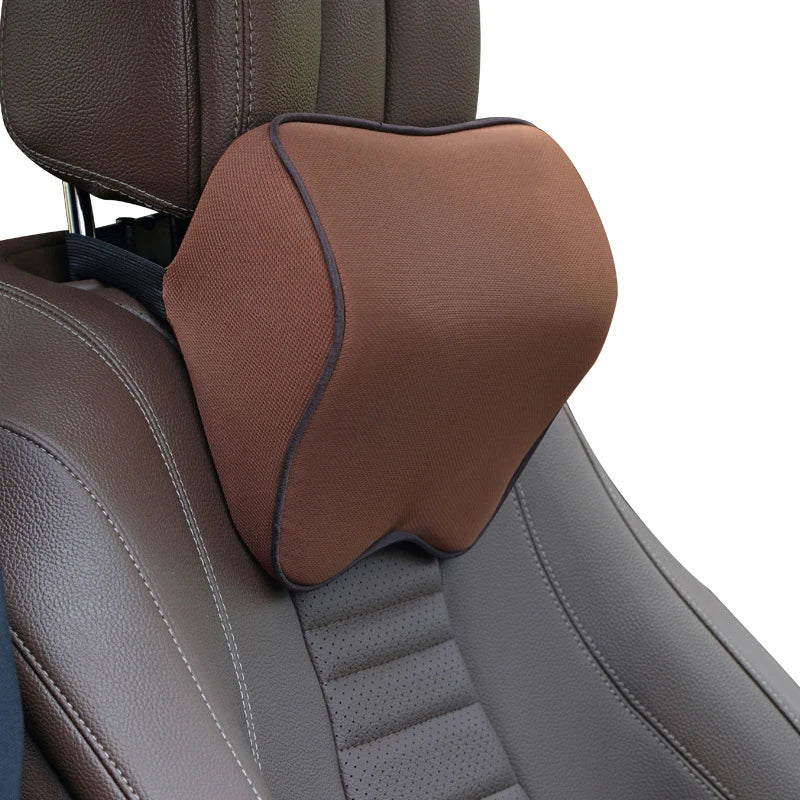 A brown memory foam car headrest neck pillow with an adjustable strap is shown on a gray car seat.