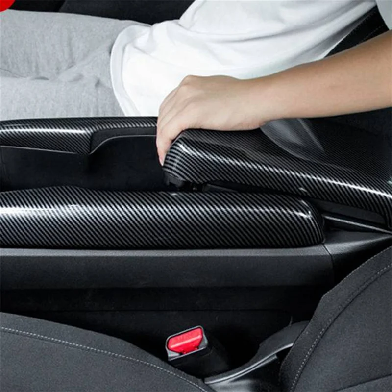 A hand is touching a black carbon fiber armrest box cover inside a car interior.