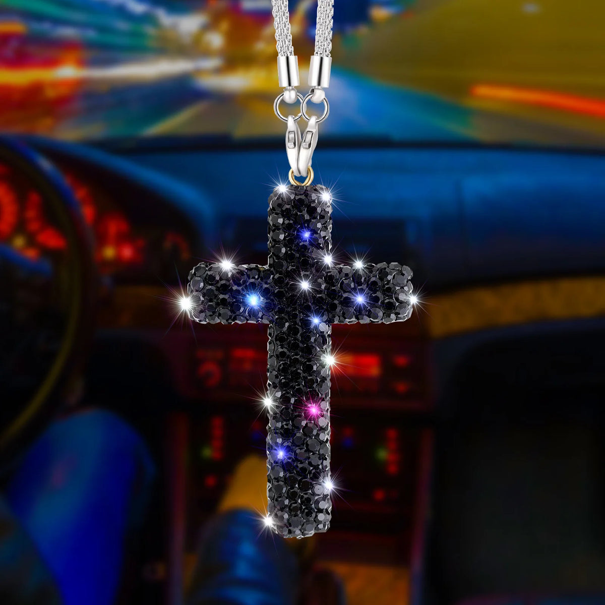 A stainless steel cross pendant with sparkling stones hangs from a chain, set against a blurred car interior background.