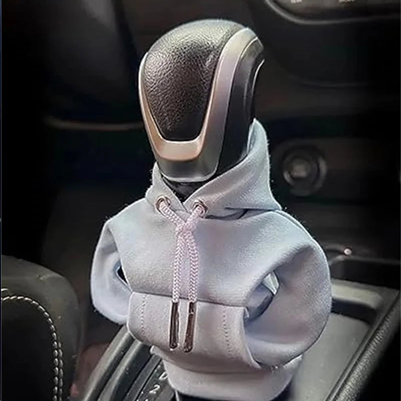 A light gray knit cover is placed over a gear shift knob in a car interior.