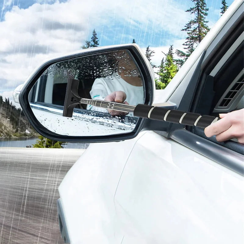 A hand uses a wooden glass cleaning tool to wipe the exterior of a car window.