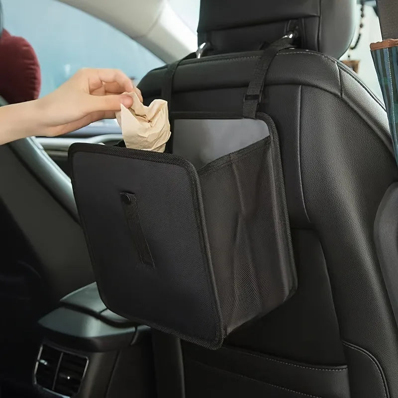 A hand places a tissue into the storage compartment of a black car trash organizer.