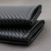 A close-up of a folded black carbon fiber seat belt shoulder pad cover.