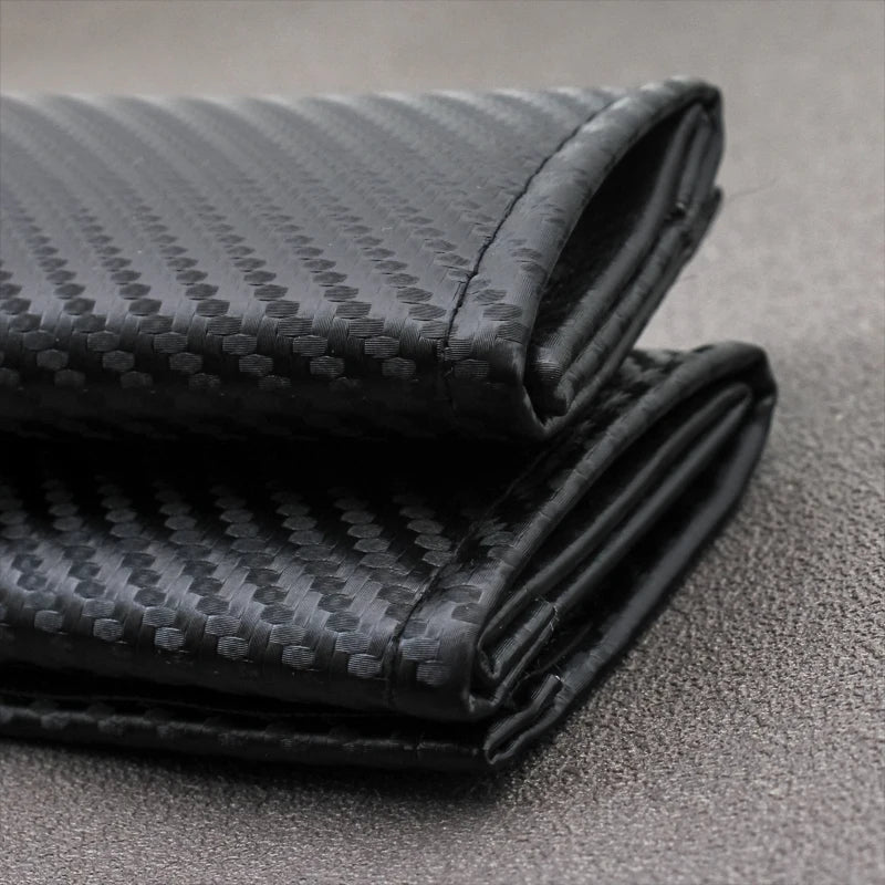 A close-up of a folded black carbon fiber seat belt shoulder pad cover.