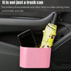 A pink portable car trash can with a hanging lid is placed in a car interior, holding a mobile phone and an umbrella.