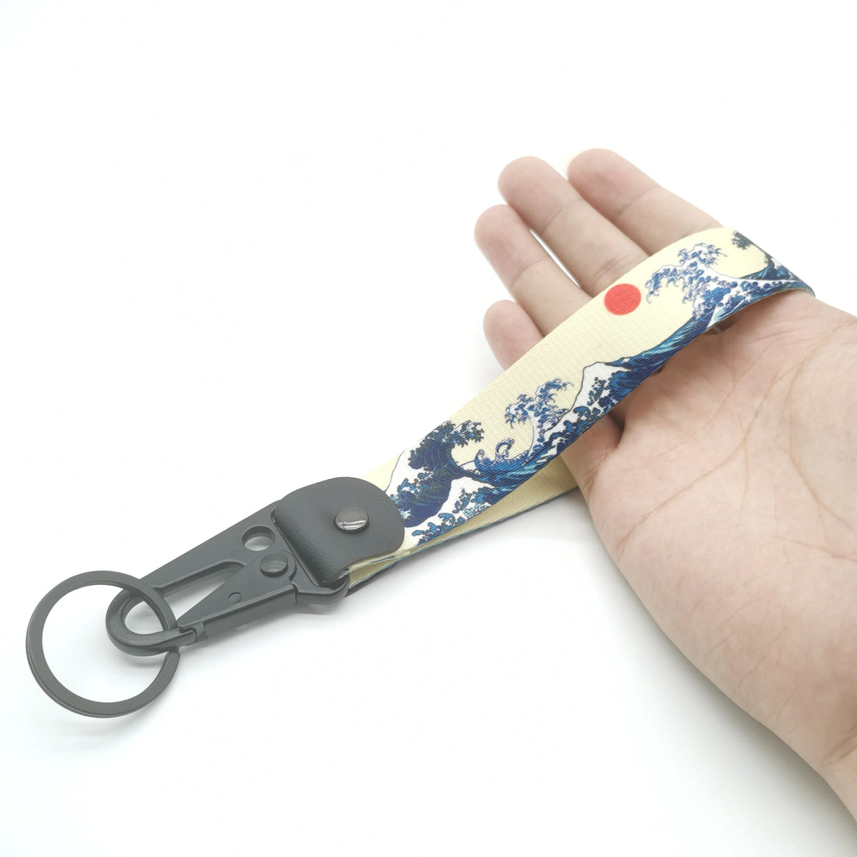 A hand holds a black keychain lanyard with a light yellow fabric featuring a blue wave pattern and a red circular accent.