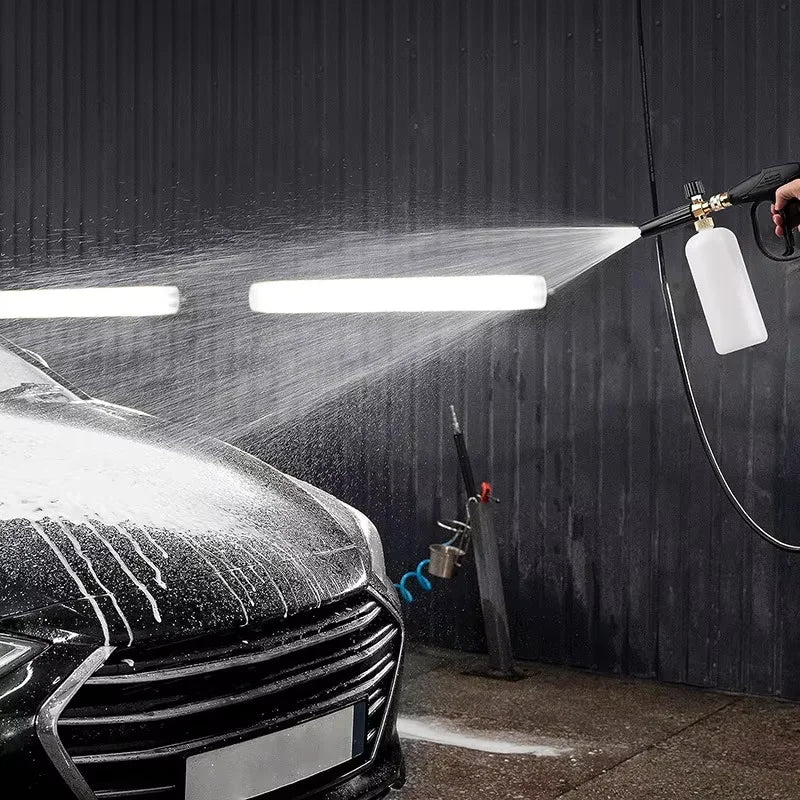 A high-pressure cleaning gun sprays water onto a car's surface in a dark garage setting.