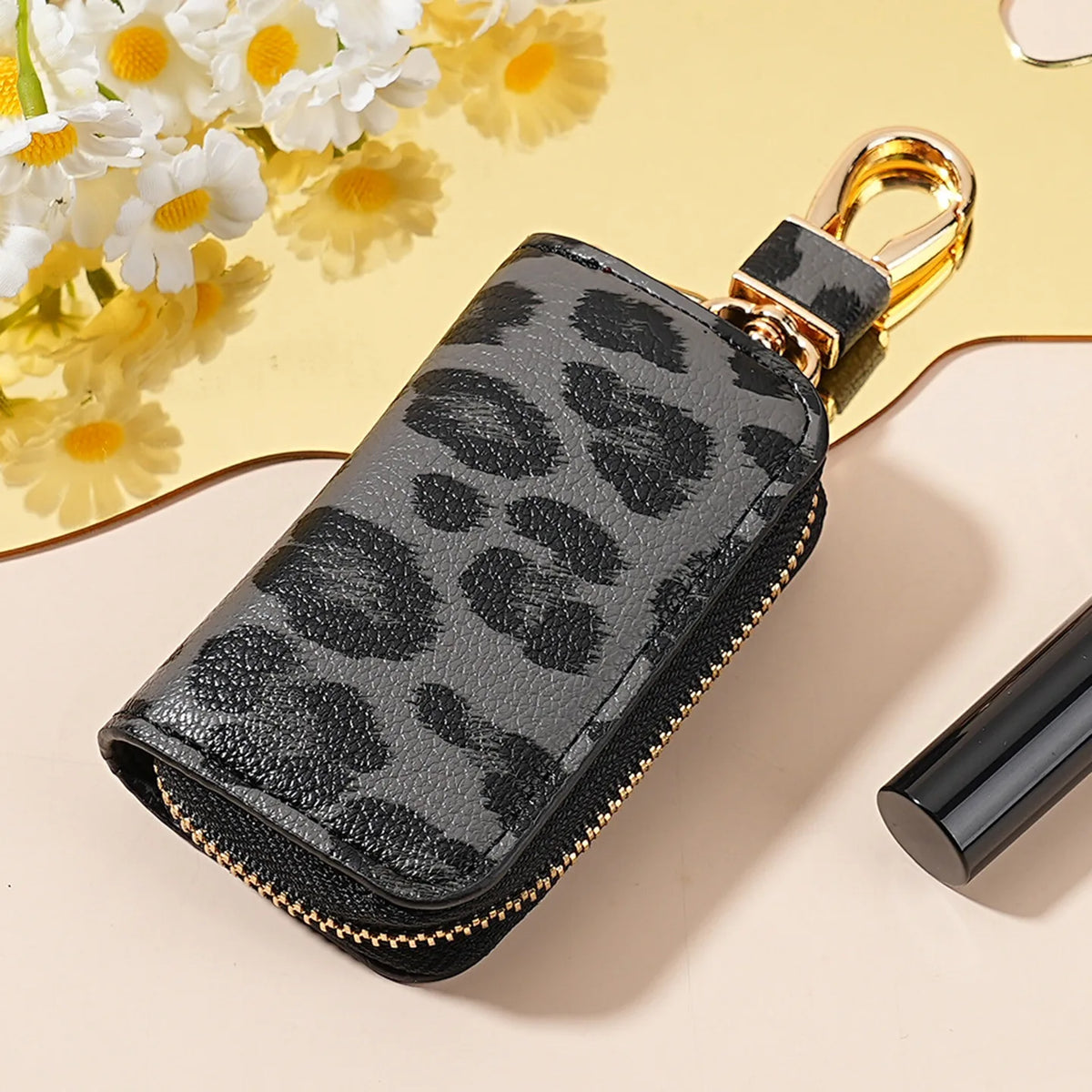 A black leopard print car key holder with a gold-colored clasp resting on a light background.