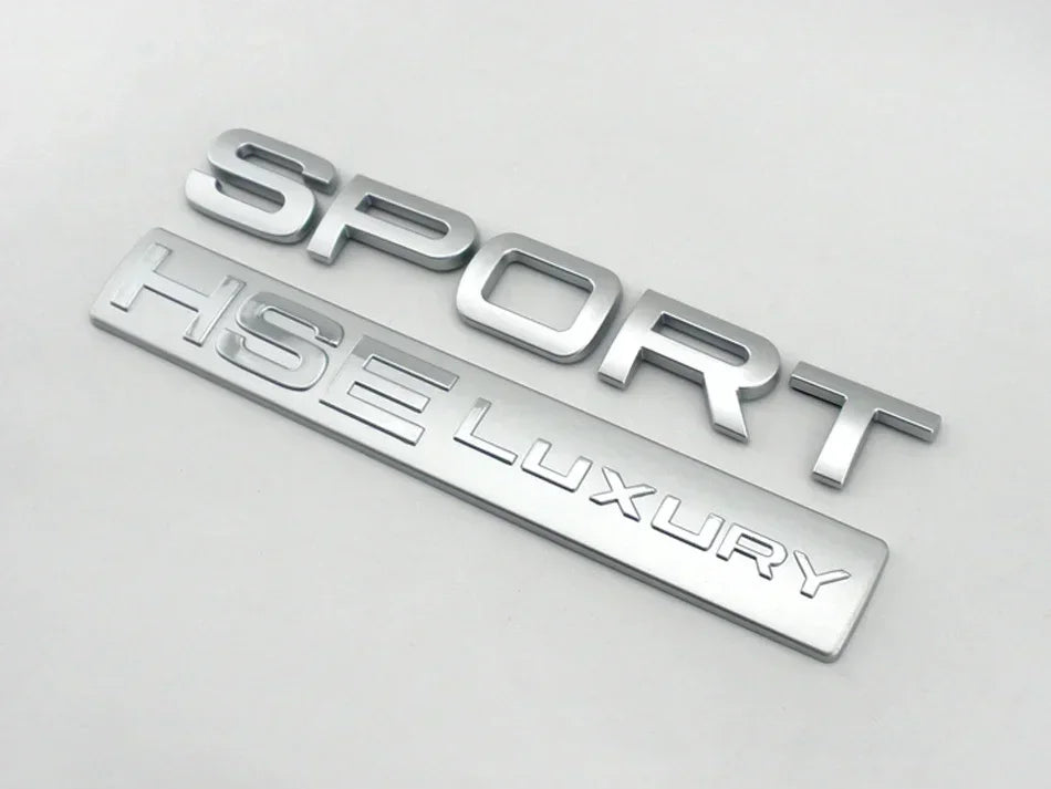 Silver metal badge spelling out SPORT LUXURY for a car decal.