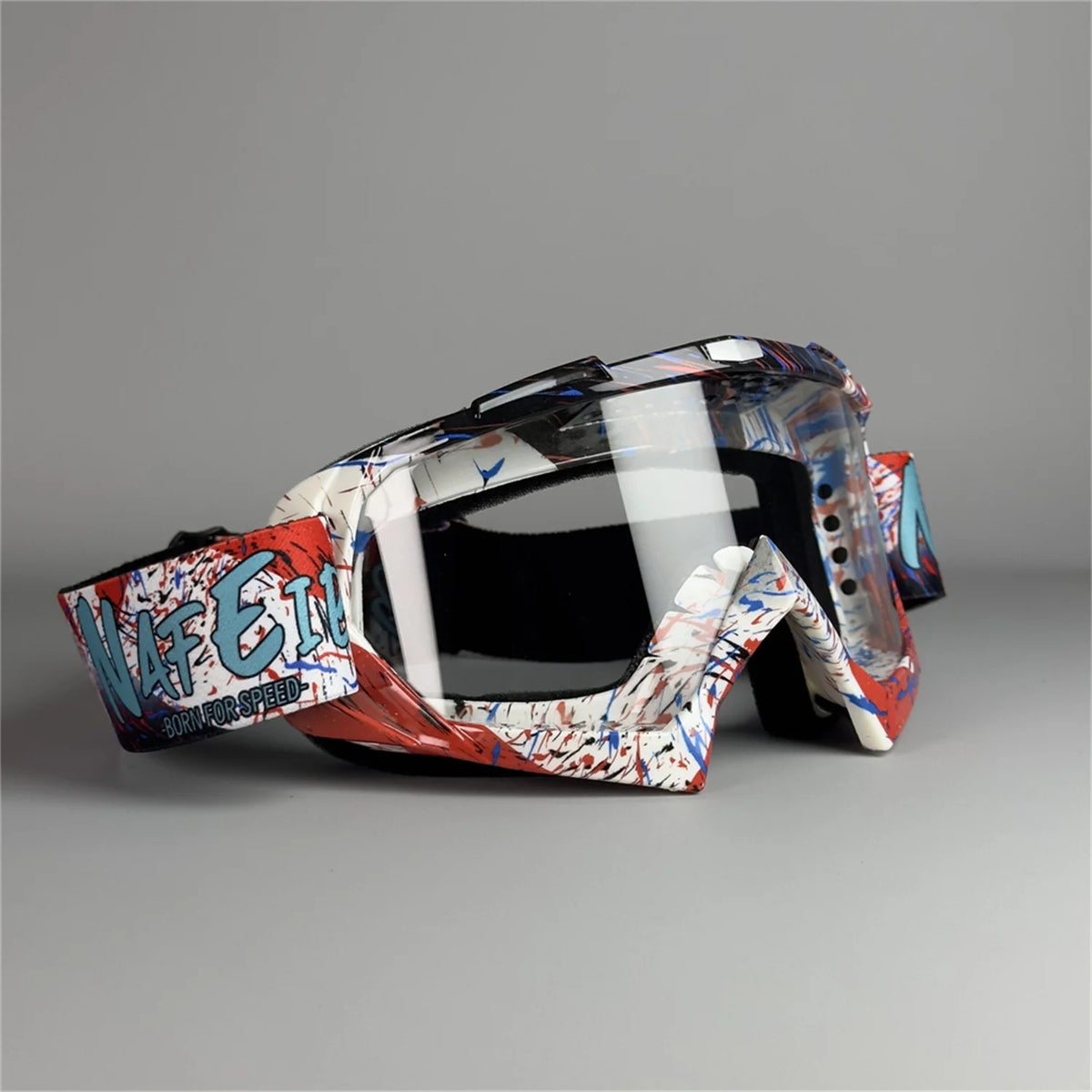 Un par de gafas de motocicleta con patrón rojo, blanco y azul sobre una superficie gris.