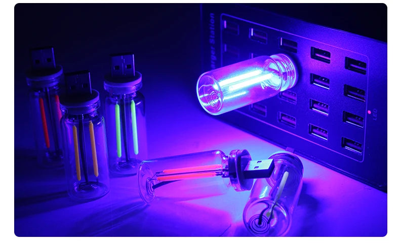 Eine Ansammlung von Glasröhrchen mit leuchtenden Flüssigkeiten werden neben einem blauen elektronischen Panel präsentiert.