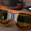 A pair of brown leather retro folding motorcycle windproof glasses resting on a wooden surface.