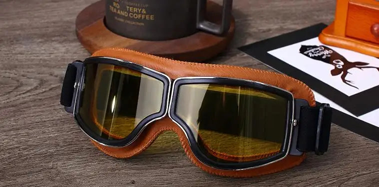 A pair of brown leather retro folding motorcycle windproof glasses resting on a wooden surface.