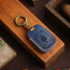 A dark blue leather key cover with a brass ring is placed on a wooden box.