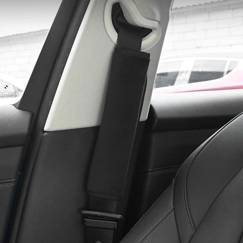Black and white dual plush seat belt covers and shoulder pads installed in a car interior.
