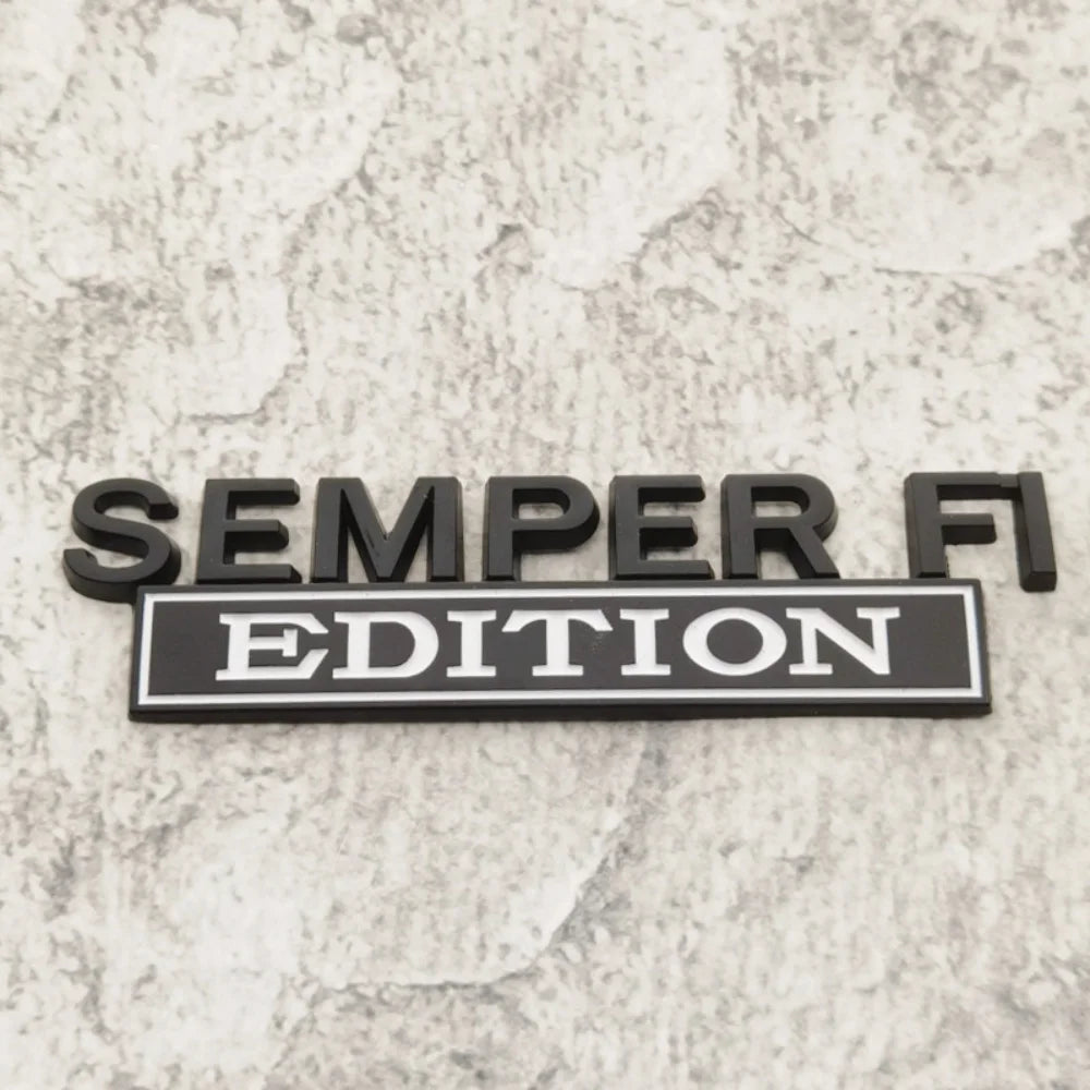 A black metal emblem with the text SEMPER FI EDITION is displayed on a light gray, textured surface.