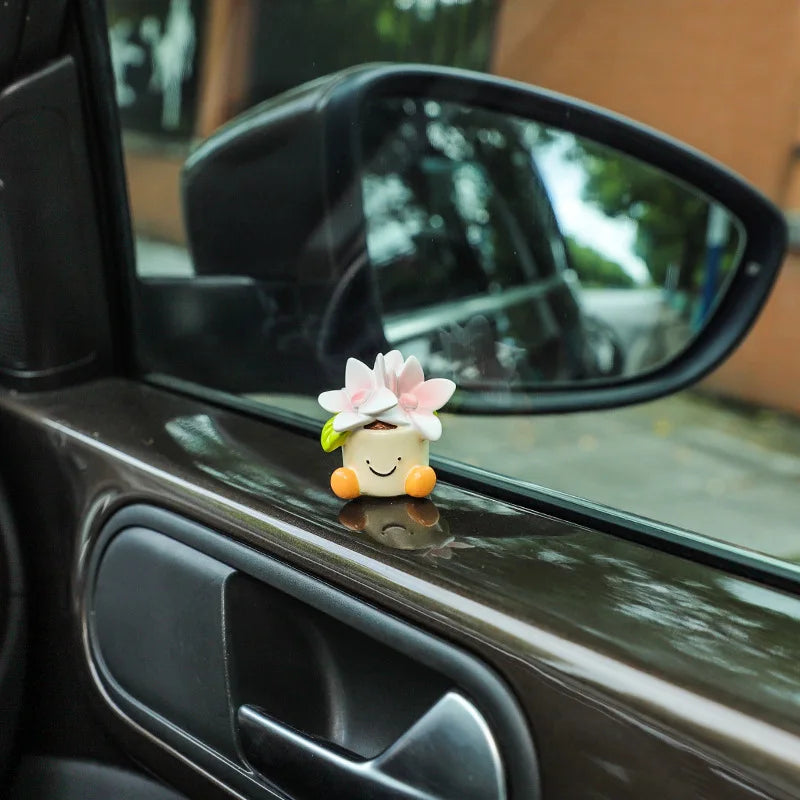 Eine kleine weiße Harzblumen-Topf-Elfen-Auto-Dekoration ruht auf einer dunklen Autofensterbank.