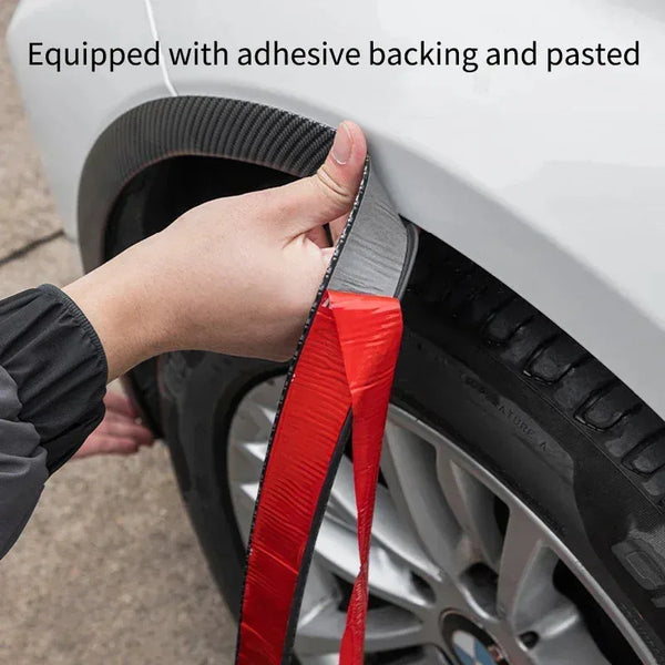 A hand is applying a red carbon fiber trim piece with adhesive backing to a car wheel arch.
