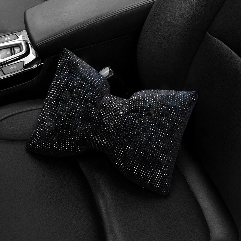 Almohada de cuello para coche de cristal de imitación con pedrería negra sobre un asiento oscuro de coche.